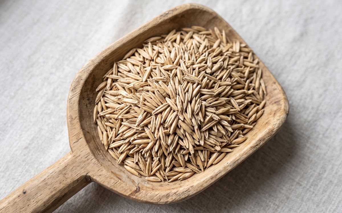 Raw oat kernels with hulls heaped in a wooden scoop